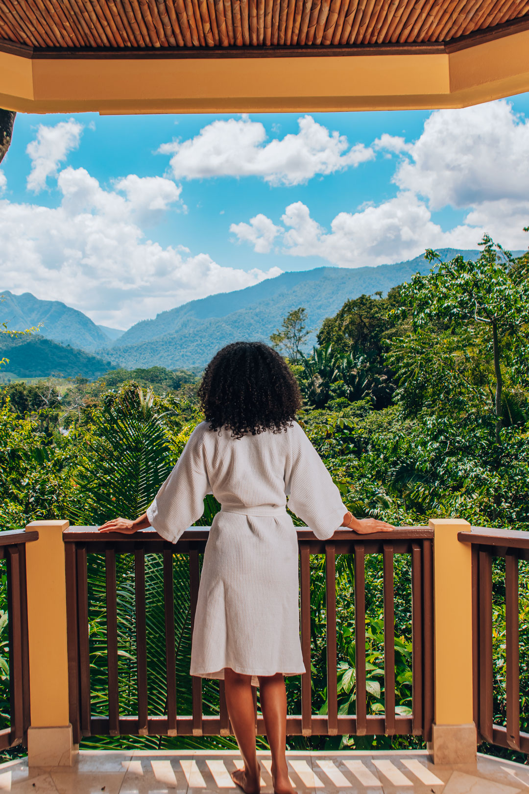 A woman standing on the front balcony looking at the jungle and mountains at The Rainforest Lodge at Sleeping Giant