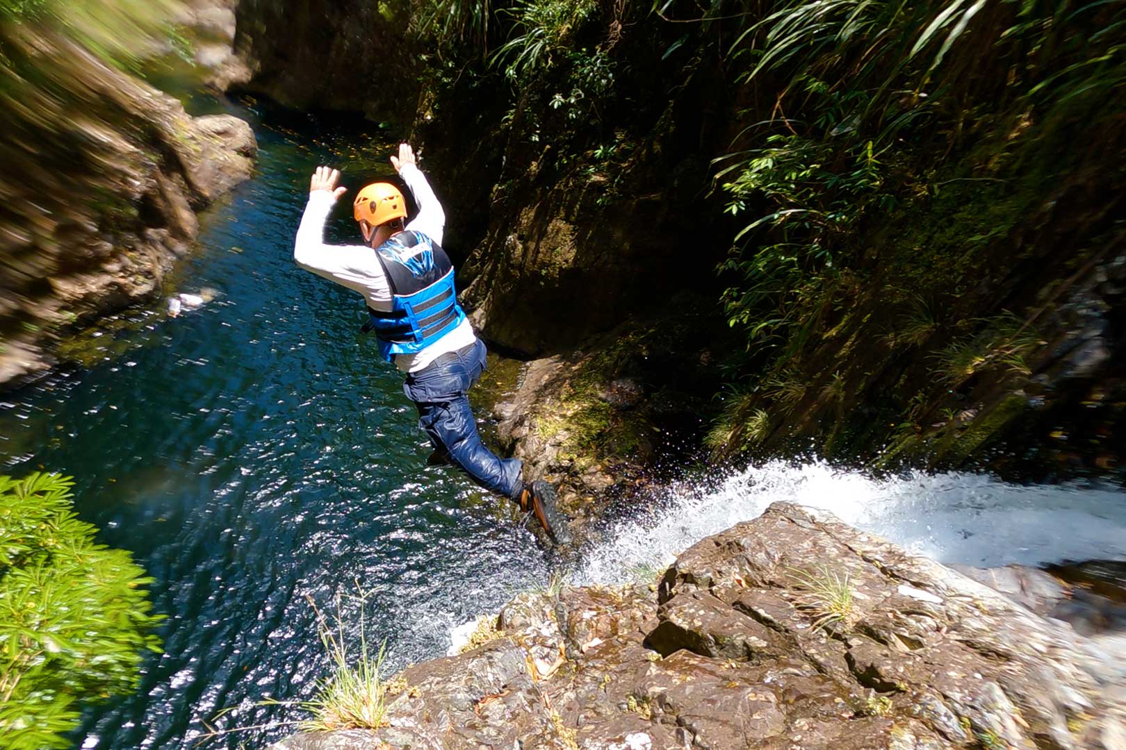 A guest jumping off the top of the waterfall into the pool below at The Waterfall Expedition at The Rainforest Lodge at Sleeping Giant