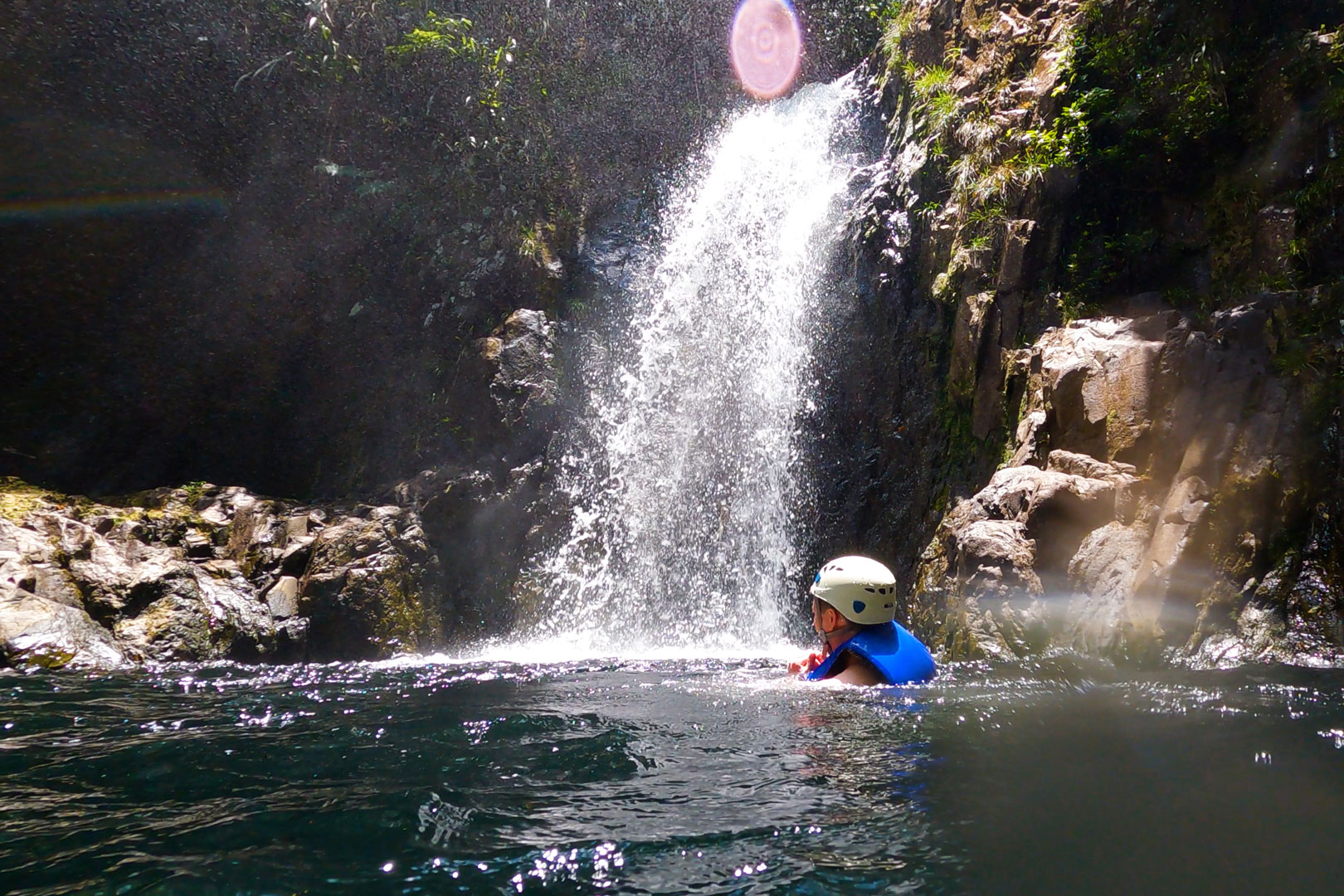 A guest swimming in the pool under the waterfall at The Rainforest Lodge at Sleeping Giant