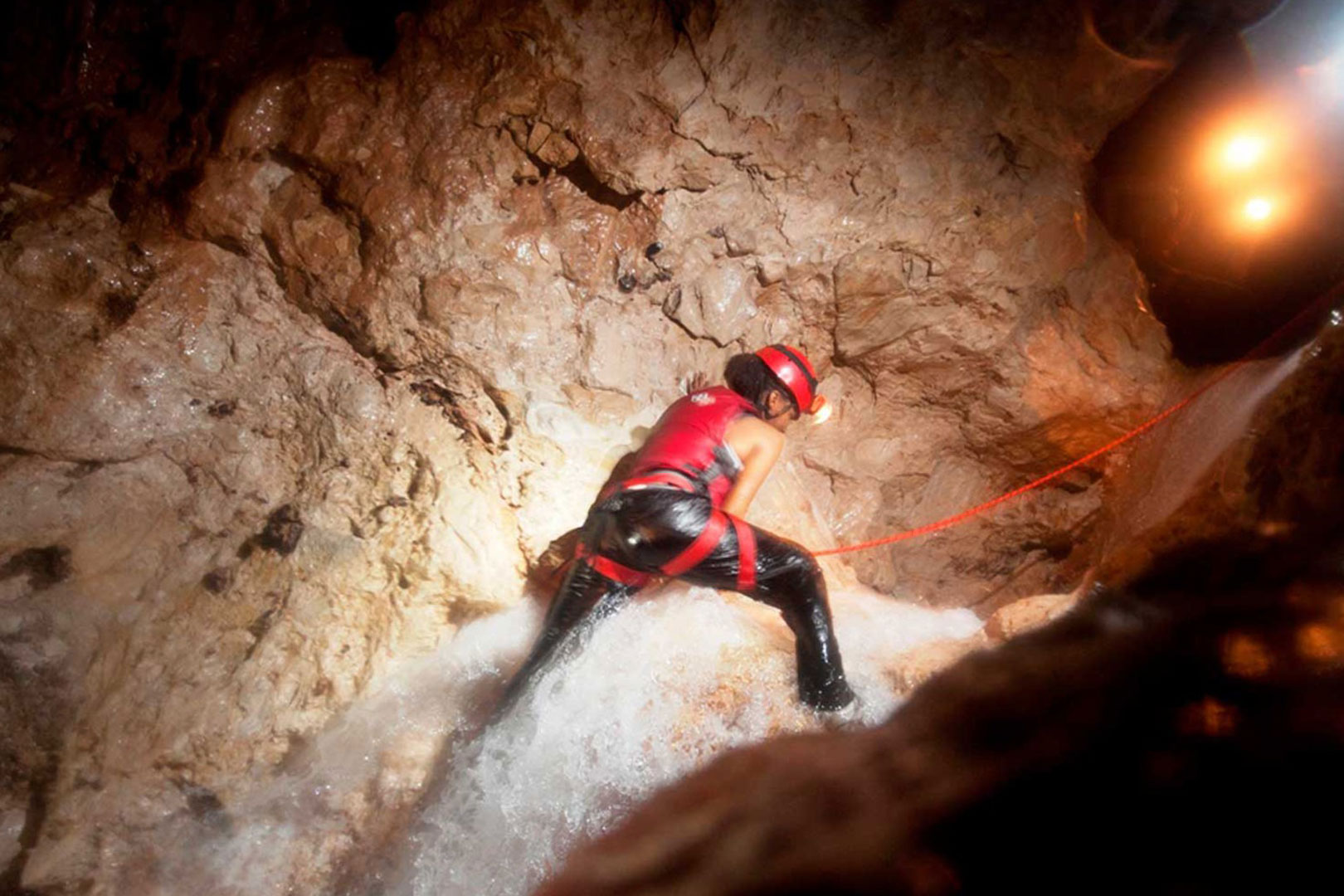 A a guest climbing one of the waterfalls during the Waterfall Cave expedition at The Rainforest Lodge at Sleeping Giant