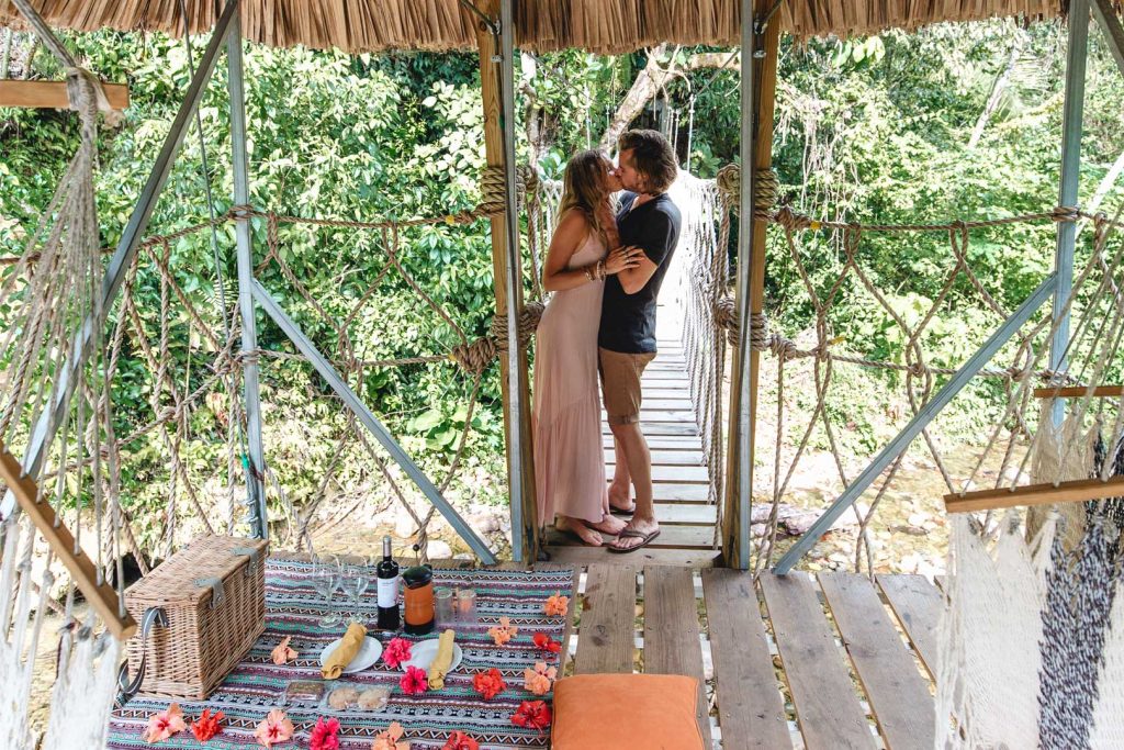 A couple kissing on a rope bridge at The Rainforest Lodge at Sleeping Giant