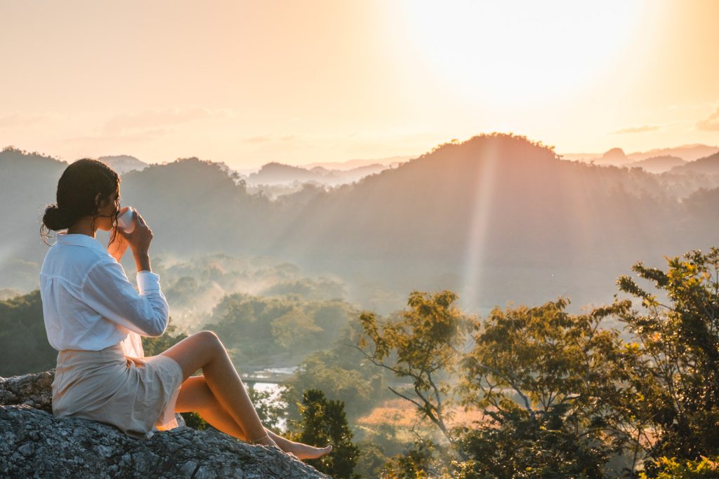 A woman sitting on a rock watching the sunrise from behind the mountains at The Rainforest Lodge at Sleeping Giant