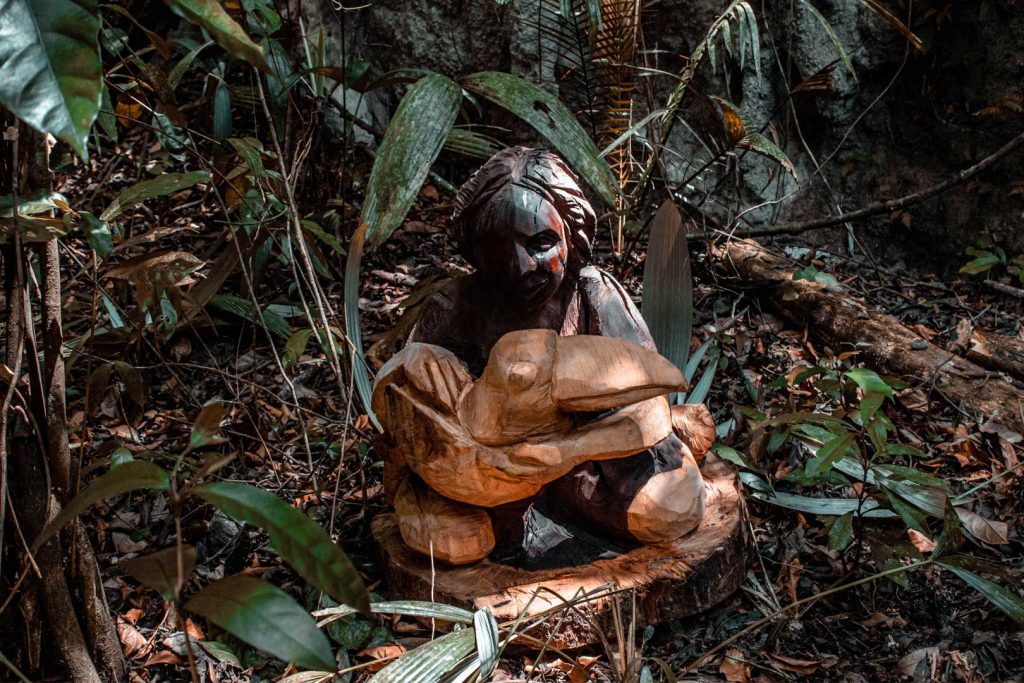 A wooden sculpture of woman holding a toucan in the forest at The Rainforest Lodge at Sleeping Giant