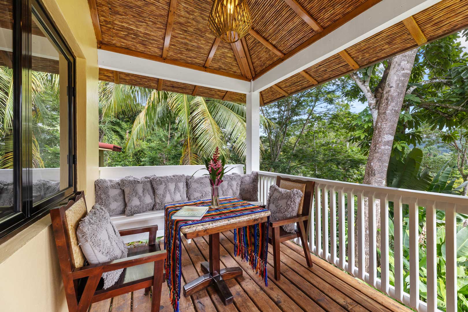The private balcony with a small table, two arm chairs and a wooden bench outside of the Jungle Cottage with Plunge Pool at The Rainforest Lodge at Sleeping Giant